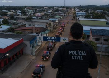 Policial civil de costas, com viaturas em uma rua de Urupá.