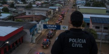 Policial civil de costas, com viaturas em uma rua de Urupá.