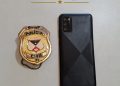 Celular preto ao lado de um distintivo da Polícia Civil de Rondônia.