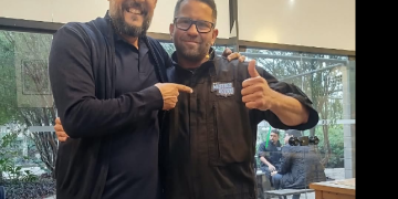 Evelton Silva, conhecido como Polaco, usa uniforme do reality Mestres do Frio ao lado de outro homem.